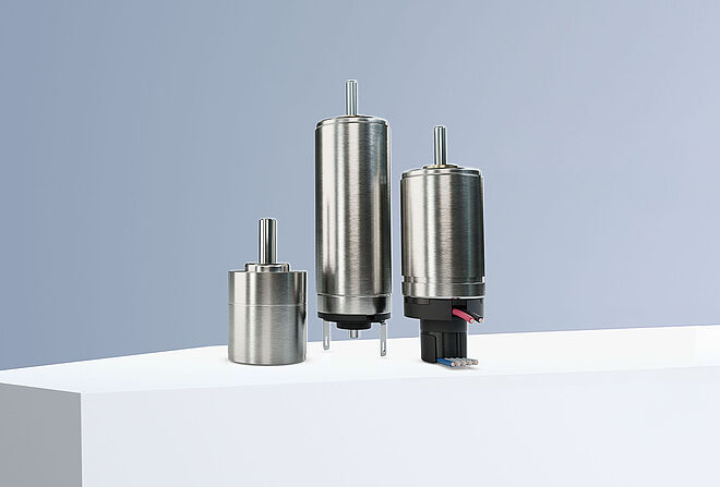 两台来自 FAULHABER SXR 和 GXR 产品系列的直流电机以及一个编码器和一个来自 GPT 产品系列的减速机排列在灰蓝色背景下的白色台阶上。