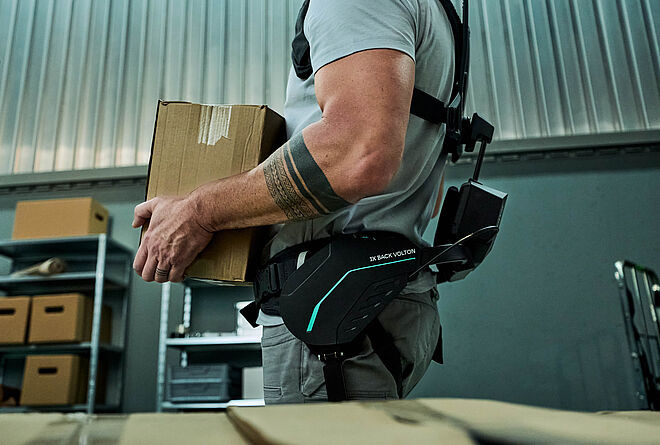 一名仓库员工在搬运箱子时佩戴 SUITX 的 IX BACK VOLTON 外骨骼，其运动辅助由集成的 FAULHABER 驱动系统实现。