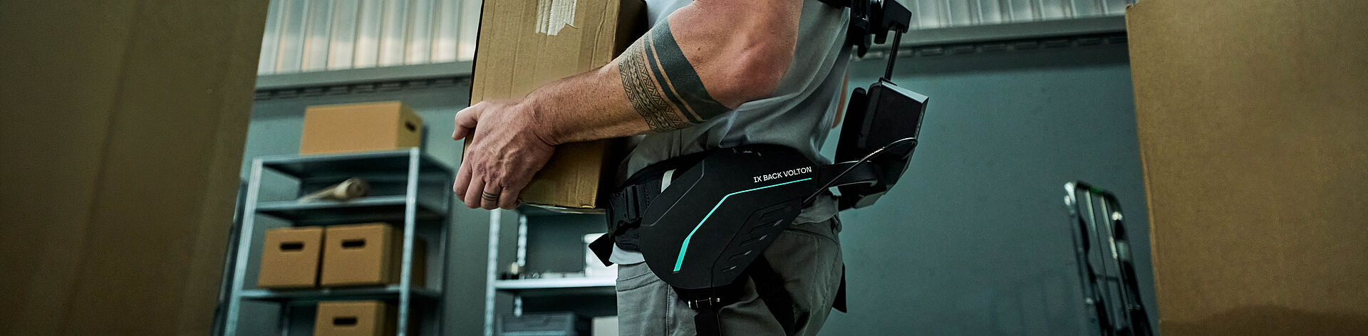 一名仓库员工在搬运箱子时佩戴 SUITX 的 IX BACK VOLTON 外骨骼，其运动辅助由集成的 FAULHABER 驱动系统实现。