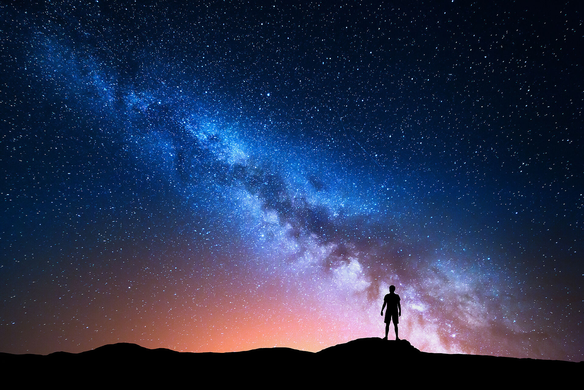 一个人站在高地上的剪影，头顶是晴朗的星空，清晰可见的银河横贯天际。该图展示了借助现代空间望远镜对宇宙进行观测的场景。