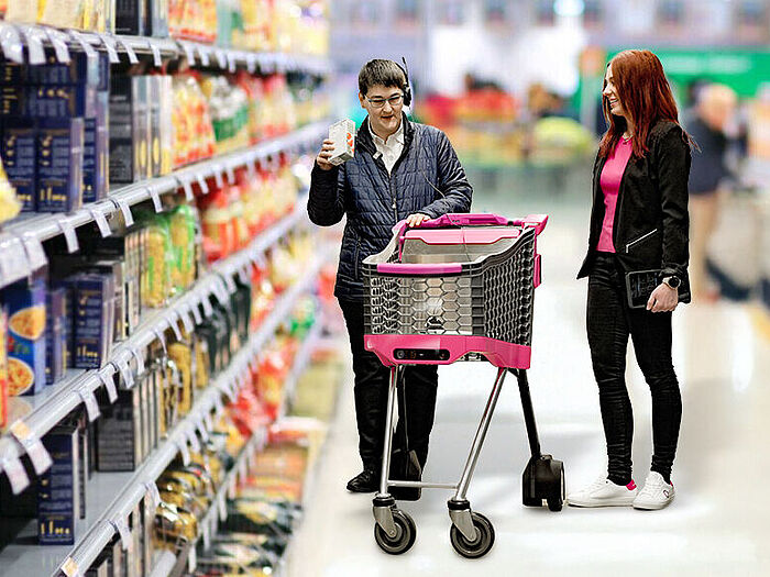 FAULHABER无刷电机应用于拉珀斯维尔应用科学大学(OST)自主购物车VIRAS项目 两个人站在超市货架之间的过道上,货架上摆满了食品包装。画面前方是“VIRAS”自主购物车(黑粉色设计),由拉珀斯维尔的OST应用科技大学开发,专为视障人士和老年人设计。