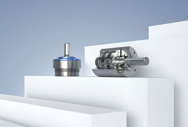 FAULHABER 生产的两个不同的小型齿轮箱，在灰蓝色背景的白色平台上排列。