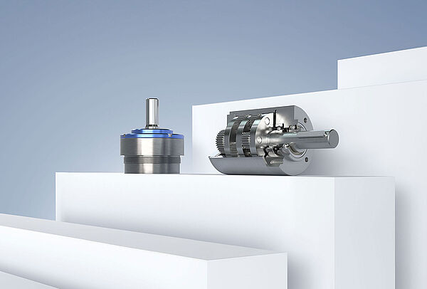 FAULHABER 生产的两个不同的小型齿轮箱，在灰蓝色背景的白色平台上排列。