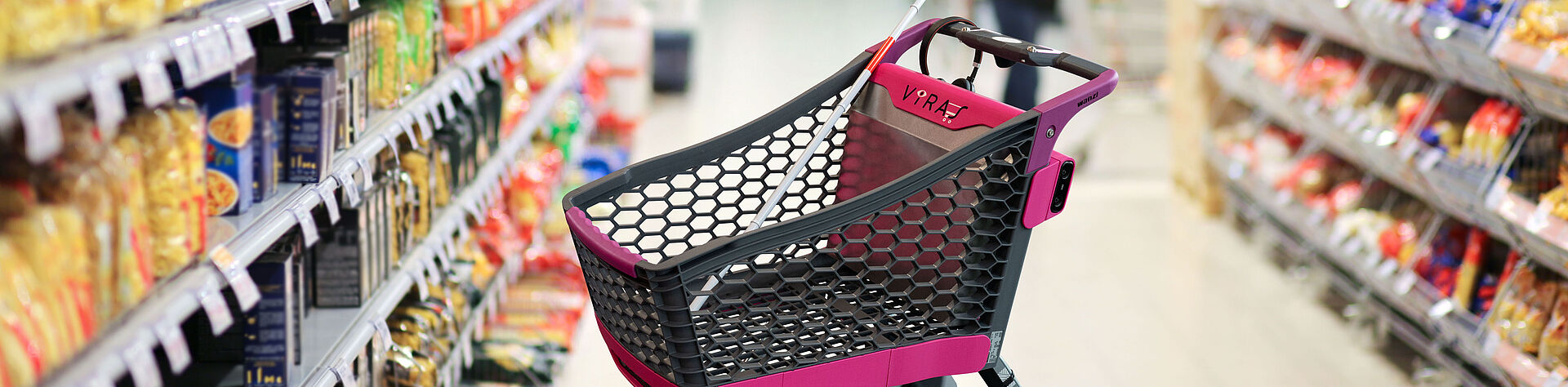 自主购物车“VIRAS”（黑色和粉色设计）的图像，该车由拉珀斯维尔的OST应用科技大学开发，位于一个明亮的超市通道中，通道两侧是摆满意面和包装食品的货架。