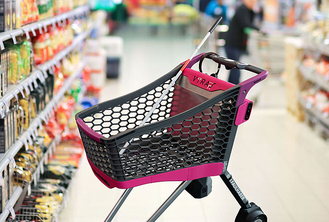 自主购物车“VIRAS”（黑色和粉色设计）的图像，该车由拉珀斯维尔的OST应用科技大学开发，位于一个明亮的超市通道中，通道两侧是摆满意面和包装食品的货架。