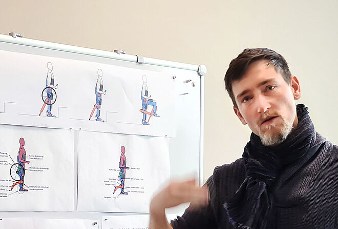 Project manager B. Eggimann reports on the “Enhanced hybrid” project; in the background is an information board with sketches of the combination of exoskeleton and wheelchair.