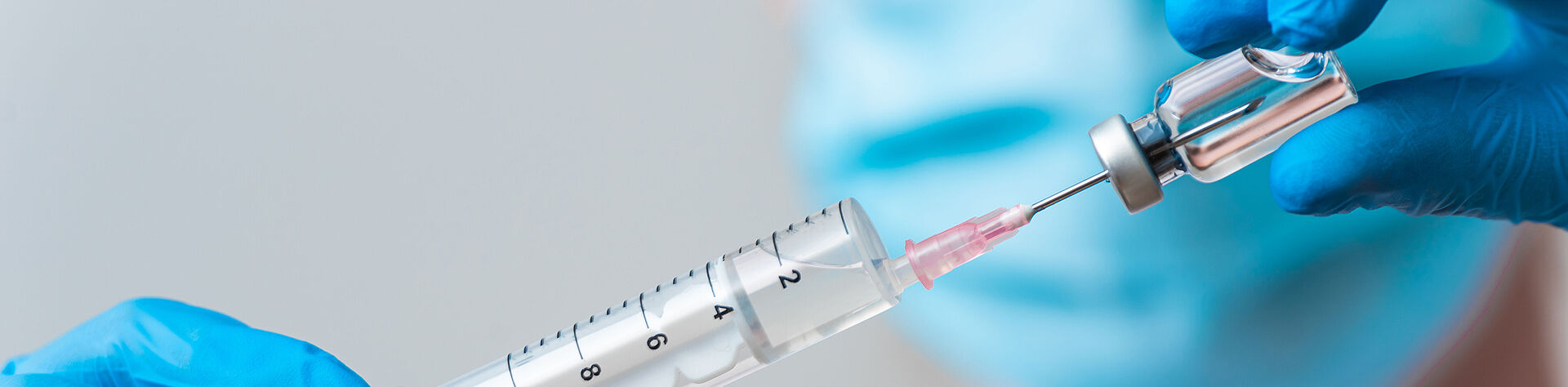 FAULHABER 无刷直流电机在自动化制药灌装系统中的应用 一名医务人员戴着口罩和手套,从容器中抽取注射器中的注射药物。